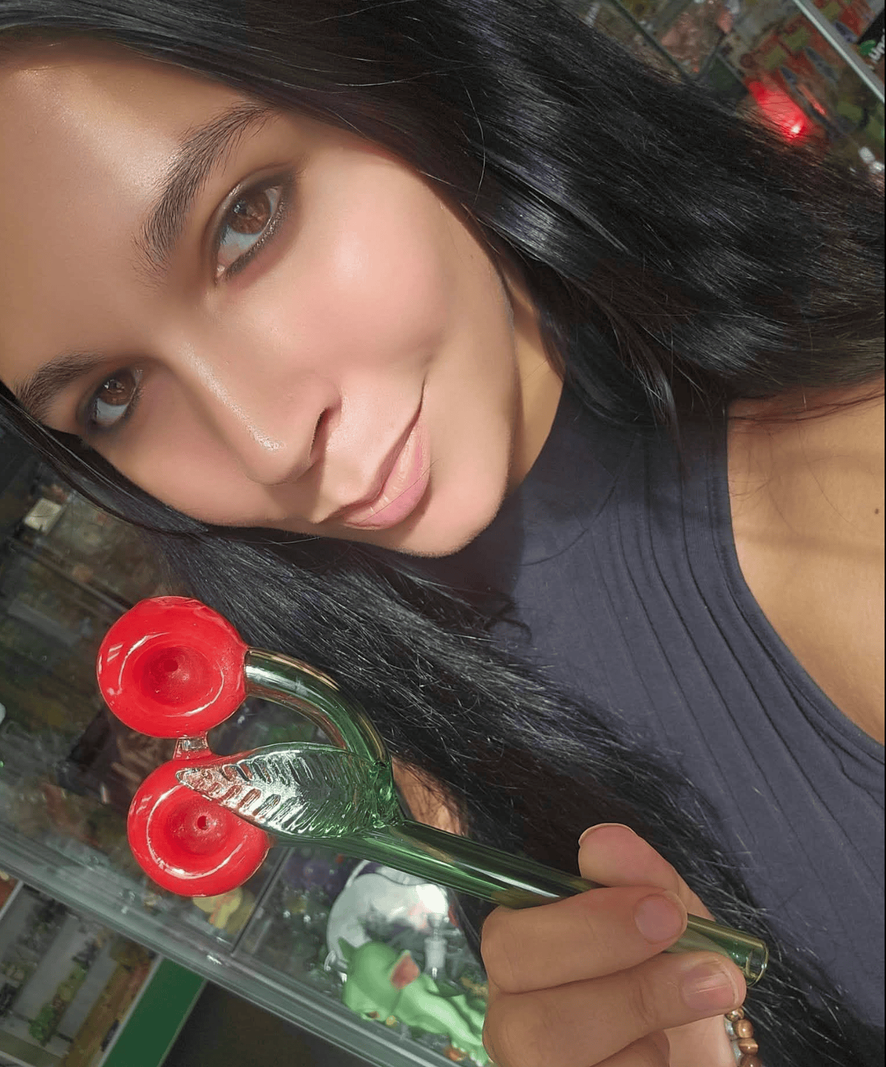 Lorette at Paradise for Adults in Centralia, WA, holding a custom double-bowl glass pipe shaped like two red cherries on a green stem.