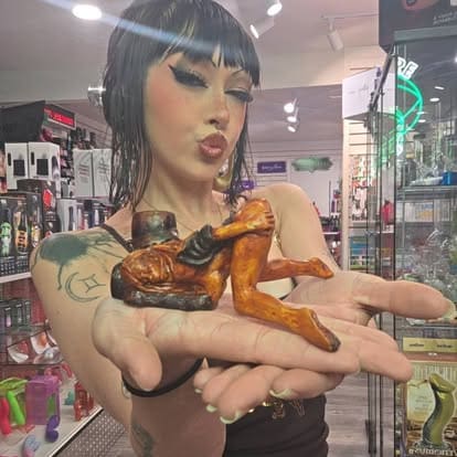 An employee named Rem at Paradise for Adults in Centralia, WA, smiles and holds out a novelty, hand-sculpted ceramic smoking pipe shaped like an erotic pin-up figure.