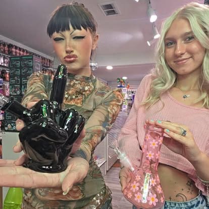 Rem and Liv holding a ceramic middle finger bong and a pink daisy glass water pipe inside Paradise for Adults in Centralia, WA.